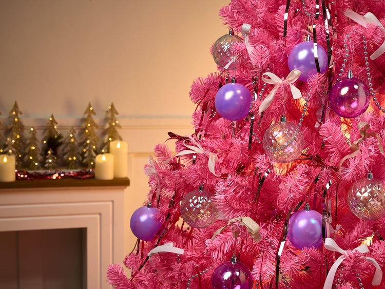 Dekorierter, pinkfarbener Weihnachtsbaum mit Christbaumkugeln und Girlanden vor einem Kamin mit Kerzen und Deko-Tannenbäumen