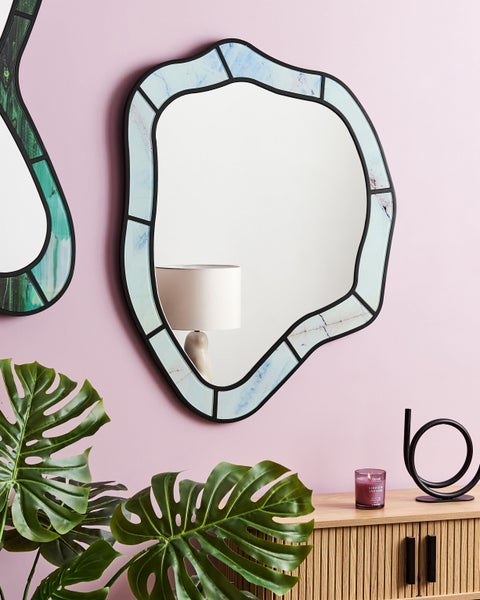 Wandspiegel mit abstraktem Rahmen über einer Kommode mit Zimmerpflanze und Dekoartikeln