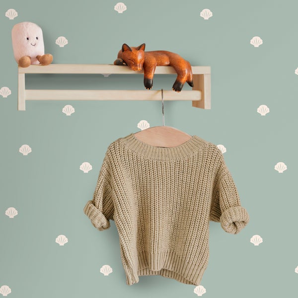 Kinderzimmerwand mit Muschel-Mustertapete, Holzregal mit Fuchsfigur und Kuscheltier sowie Strickpullover auf Holzkleiderbügel.