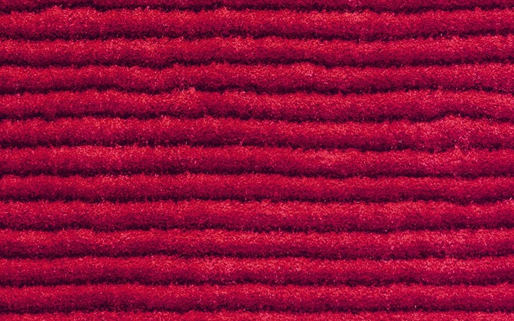 Nahaufnahme einer roten gerippten Fußmatte mit horizontaler Struktur aus Textilfasern.