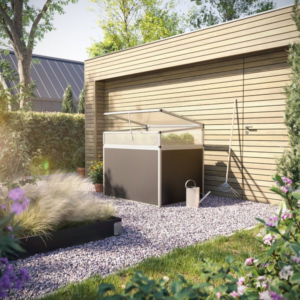 Moderner Gartenbehälter mit geöffnetem lichtdurchlässigem Deckel auf einem Kiesweg in einem Garten mit Gartenhaus und Werkzeug.