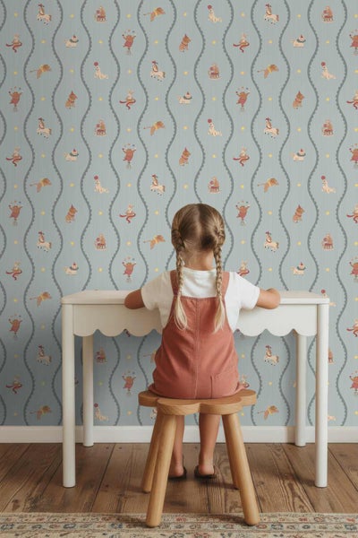 Vliestapete mit Zirkus-Motiven wie Pferden und Affen in Wellenlinien, ein Kind sitzt an einem Schreibtisch im Kinderzimmer.