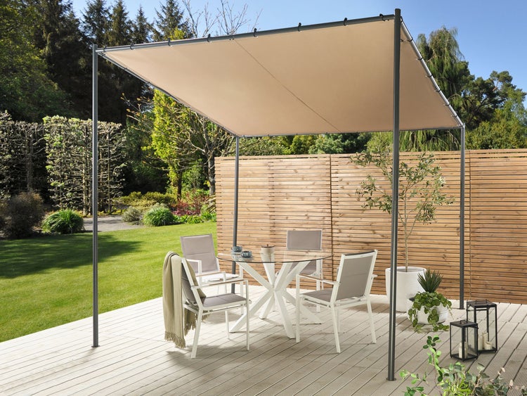 Gartenpergola mit dunklem Metallgestell und beigem Stoffdach auf einer Holzterrasse. Sitzgruppe mit Glastisch und weißen Stühlen vor einem Holzzaun.