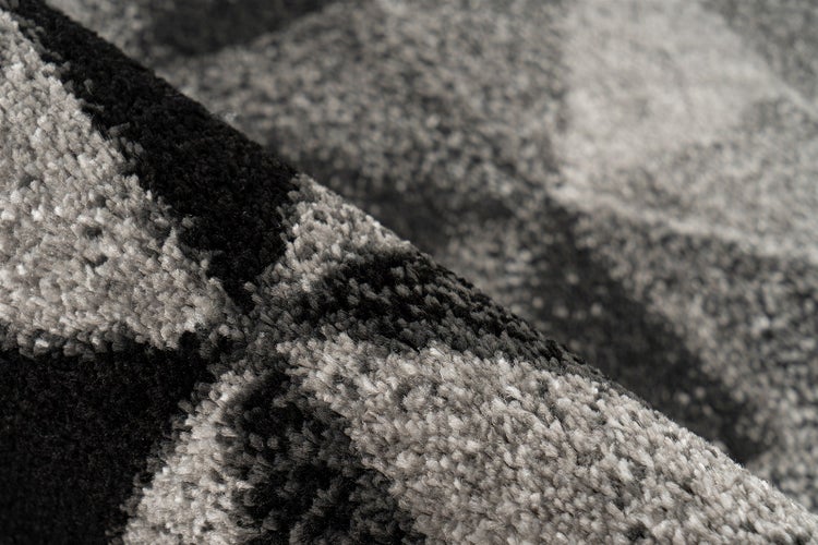 Detailansicht eines schwarz-grauen Hochflorteppichs mit geometrischem Muster und weicher Textur.