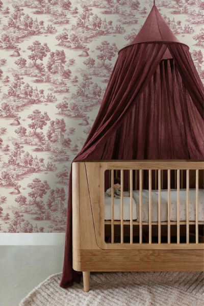 Kinderzimmer mit Toile-de-Jouy-Tapete in Weinrot und Creme sowie einem hellen Holzbabybett mit dunkelrotem Betthimmel.