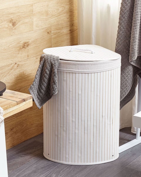 Wäschekorb aus weißen Bambus-Lamellen mit Deckel und Stoffeinlage in einem hellen Badezimmer mit Holzdekor und grauen Handtüchern.