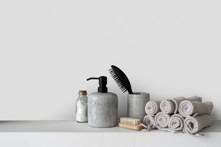 Badezimmer-Accessoires mit Seifenspender und Becher in Steinoptik, Haarbürste, Nagelbürste und einem Stapel gerollter Handtücher.