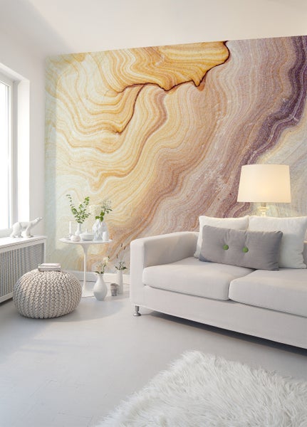 Fototapete mit Sandstein-Optik in einem hellen Wohnzimmer mit weißem Sofa, Beistelltisch und Strick-Pouf.