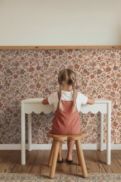 Mädchen sitzt an einem weißen Kindertisch vor einer floralen Tapete