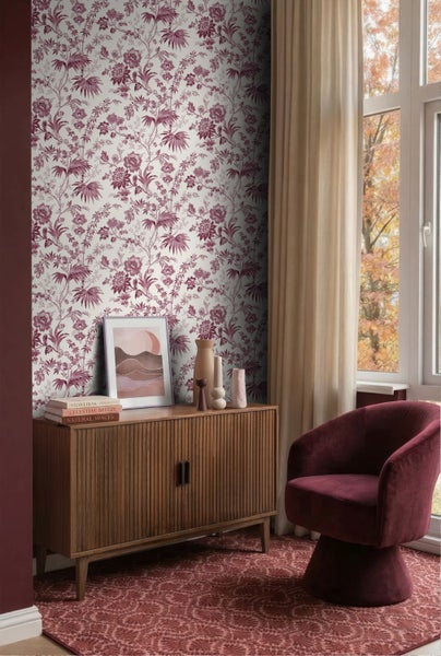 Wohnraum mit floral gemusterter Tapete, einem Sideboard aus Holz und einem burgunderroten Samtsessel vor einem Fenster.