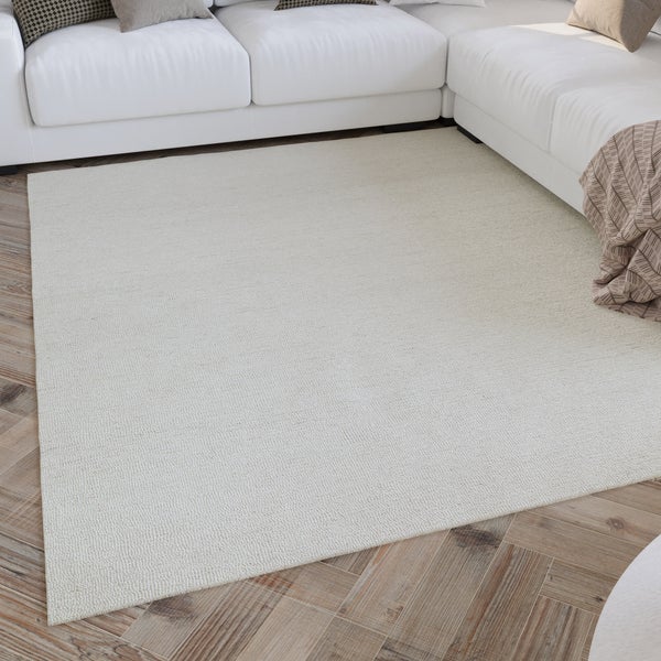 Großer, rechteckiger Teppich in Creme mit Struktur, platziert auf einem Holzparkettboden vor einem weißen Sofa in einem hellen Wohnzimmer.