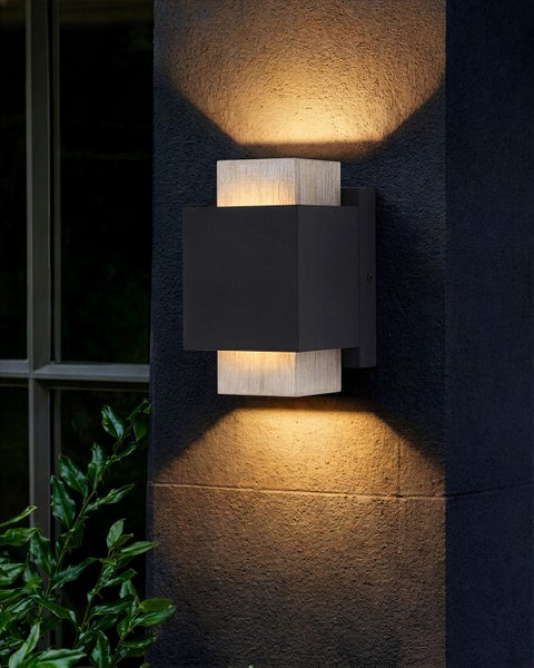 Moderne rechteckige Außenwandleuchte an einer dunklen Wand, Lichtaustritt nach oben und unten, Gehäuse in dunklem Metall und Holzoptik.