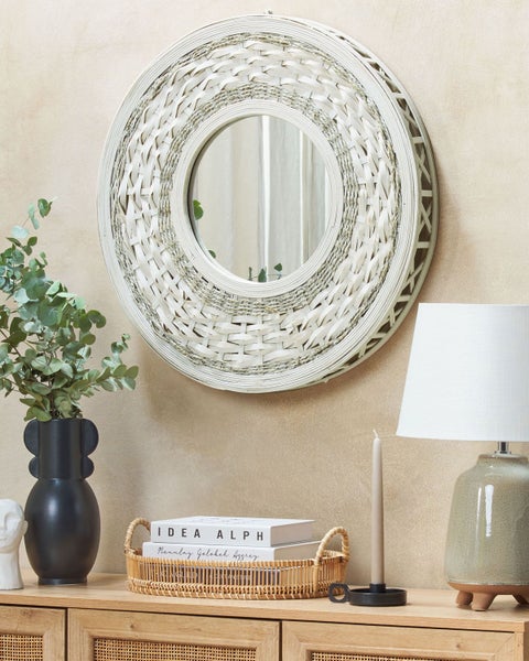 Dekoratives Interieur mit rundem Spiegel mit geflochtenem Rahmen, Tischlampe, Blumenvase und Dekoration auf einem Holzschrank