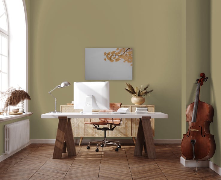 Ein modern eingerichtetes Arbeitszimmer mit olivgrüner Wandgestaltung, Schreibtisch, Computer, Ledersessel, Kommode und einem Cello.