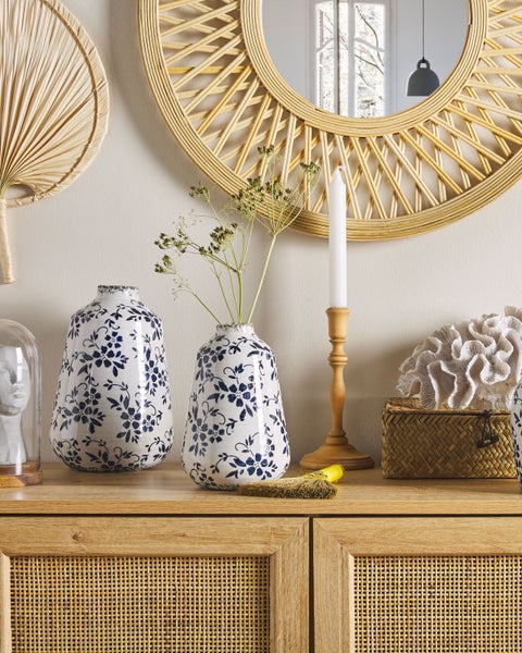 Dekorative Szene mit Spiegel, Vasen, Kerzenhalter und Kommode aus Rattan.