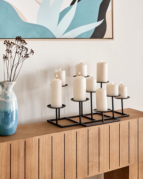 Dekoratives Arrangement mit Kerzenleuchter, Kerzen und Vase auf einem Holzmöbelstück.