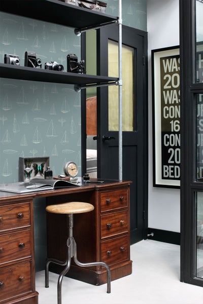 Vliestapete mit Segelboot-Muster in einem organisierten Arbeitszimmer mit Holzschreibtisch, Metallhocker und Regalen im Industrie-Stil.