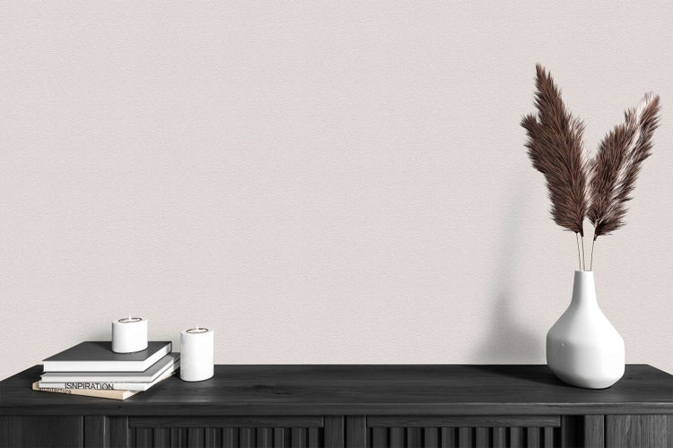 Moderne Innenszene mit fein strukturierter beiger Tapete. Ein dunkles Sideboard aus Holz mit Büchern, zwei Kerzen und einer Vase mit Pampasgras.