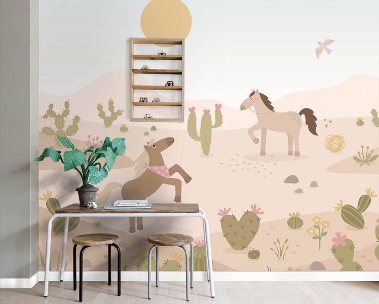 Kinderzimmer mit Vlies-Fototapete einer Wüstenlandschaft mit Pferden und Kakteen, Schreibtisch und Holzhockern.