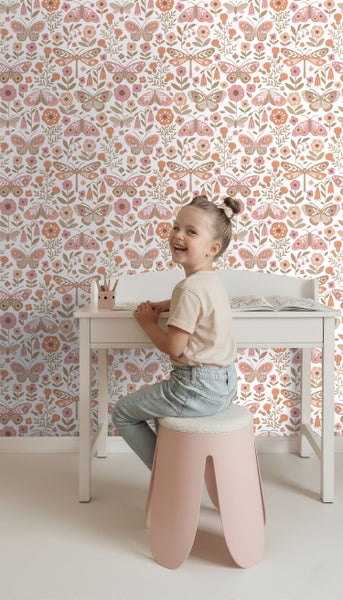 Mädchen sitzt an einem Schreibtisch vor einer Tapete mit Blumen- und Schmetterlingsmuster.