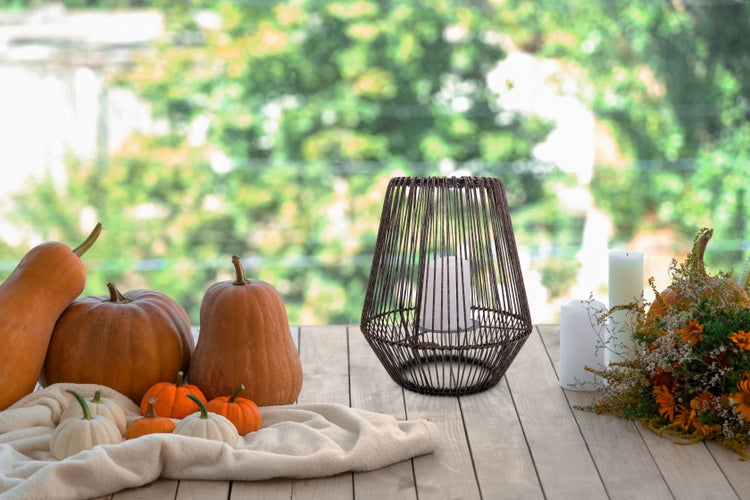 Dekorative Herbstszene mit Kürbissen, Kerzen und Windlicht auf einem Holztisch