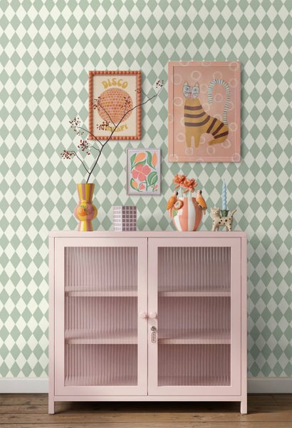 Vliestapete mit grün-weißem Rautenmuster hinter einem rosafarbenen Glasschrank mit Dekoration in einem hellen, modern eingerichteten Raum.