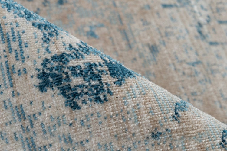 Nahaufnahme eines Teppichs mit blauem abstraktem Muster auf beigem Grund, gewebte Textur.