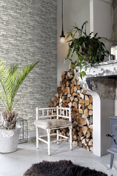 Gemütlicher Wohnbereich mit Steinwand, Holzstapel am Kamin, Zimmerpflanzen und einem dekorativen Teppich