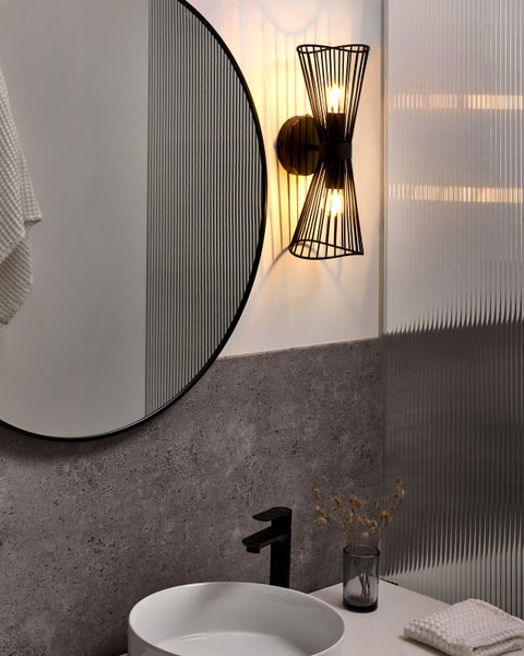 Modernes Badezimmer mit rundem Spiegel, schwarzer Wandleuchte und Waschbecken