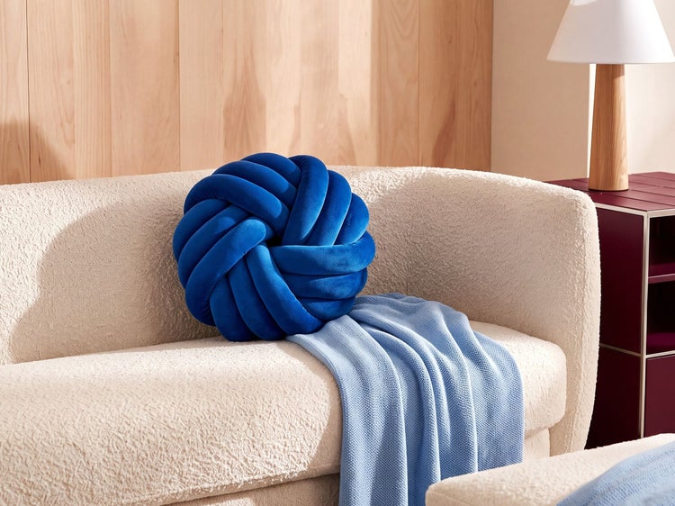 Blaues Knotenkissen in runder Form auf einem hellen Sofa mit einer hellblauen Decke in einem modernen Wohnzimmer