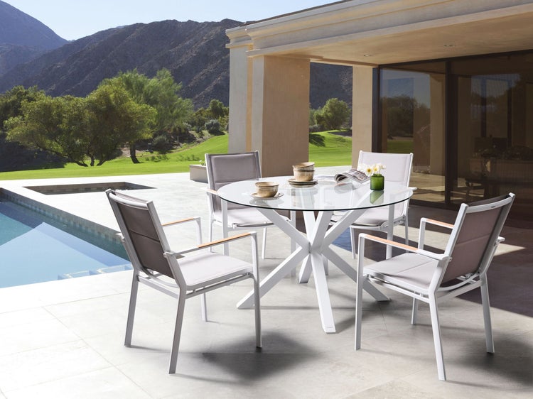 Gartenszene mit einem runden Tisch aus Glas, umgeben von vier Stühlen auf einer Terrasse mit Poolblick und Bergkulisse