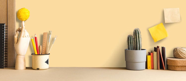 Organisierter Arbeitsplatz mit hölzerner Gliederhand, Schreibutensilien in einem Becher, Kaktus im Topf, Büchern und Haftnotizen.