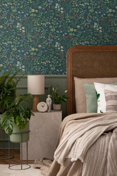 Schlafzimmer mit floraler Tapete, Bett, Nachttisch und Pflanzen