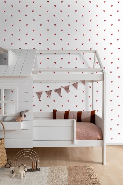 Kinderzimmer mit weißem Bett, Wand mit Herzmuster und Spielzeug