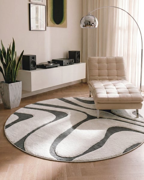 Runder Teppich mit abstraktem Muster in einem modern eingerichteten Wohnzimmer mit beiger Recamiere, Sideboard und Bogenlampe.