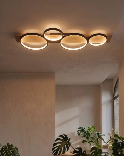 Moderne Deckenleuchte mit Holz und vier ringförmigen LED Leuchtmitteln in einem stilvollen Wohnraum mit Zimmerpflanzen.