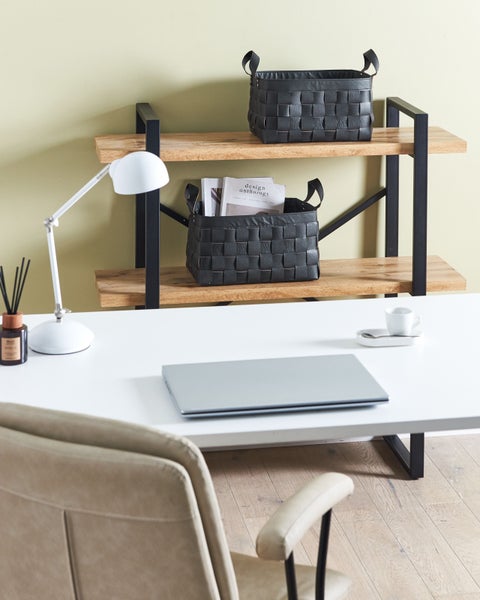 Hell eingerichteter Arbeitsplatz mit weißem Schreibtisch, Laptop und Holzregal mit zwei schwarzen geflochtenen Aufbewahrungskörben.