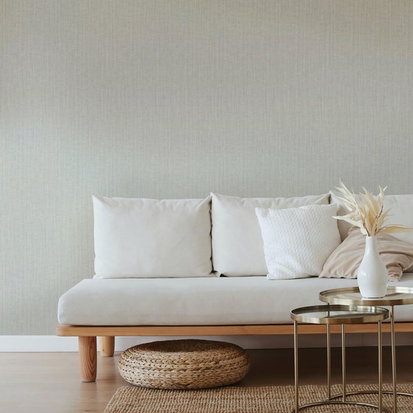 Modernes Wohnzimmer mit strukturierter Tapete in Hellgrau, weißem Sofa, Satztischen aus Metall und einem Jute-Teppich.
