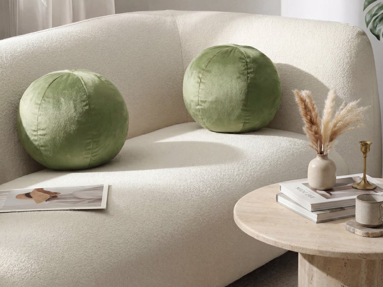 Zwei grüne kugelförmige Zierkissen aus Samt auf einem hellen Sofa mit einem runden Couchtisch aus Stein.