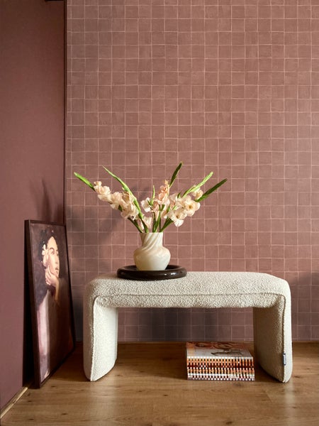 Dekoratives Interieur mit Bank, Blumen und Kunstwerk vor einer Wand mit quadratischem Muster.