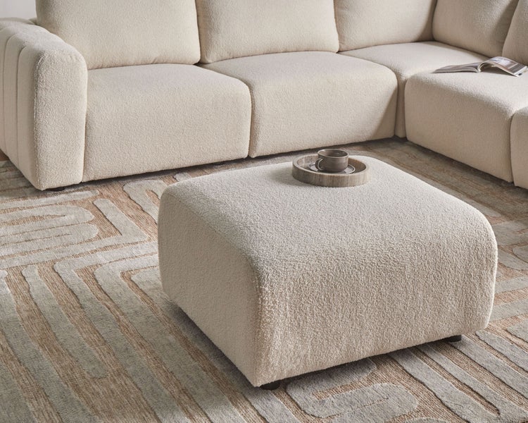 Szene mit einem Hocker, einem modularen Sofa und einem Teppich mit geometrischem Muster