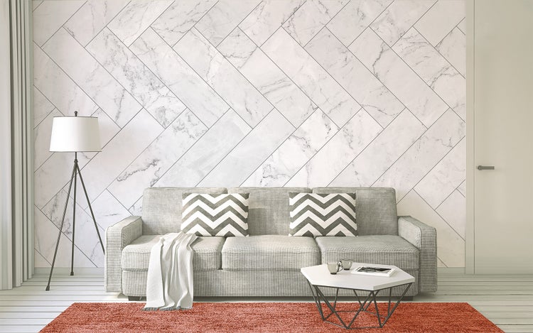 Modernes Wohnzimmer mit Wandpaneelen in Marmor-Optik im diagonalen Fischgrätmuster, einem grauen Sofa, einer Dreibein-Stehleuchte und einem Couchtisch.