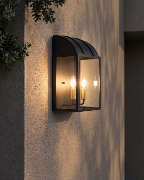 Schwarze Außenwandleuchte in Laternenform mit zwei Kerzenlampen an einer verputzten Fassade.