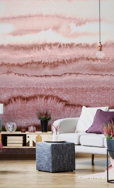 Modernes Wohnzimmer mit einer großflächigen Fototapete in Aquarell-Optik und horizontalem Verlauf. Weiße Couch, grauer Hocker und Holzsideboard.