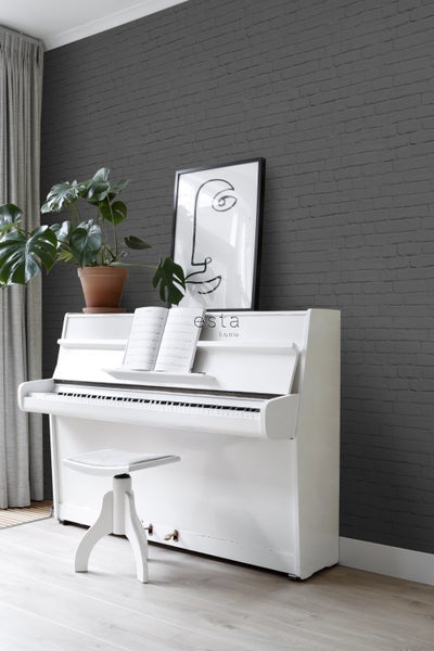 Einrichtungsidee mit weißem Klavier, Hocker, Zimmerpflanze und Wandbild vor einer Backsteinwand.
