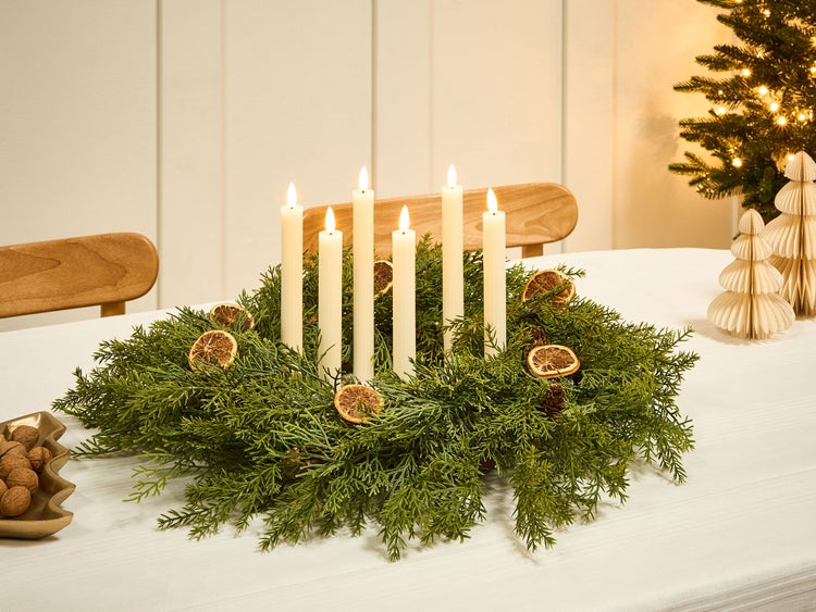 Dekorativer Adventskranz mit Kerzen, Orangenscheiben und Tannenzapfen auf einem Tisch.