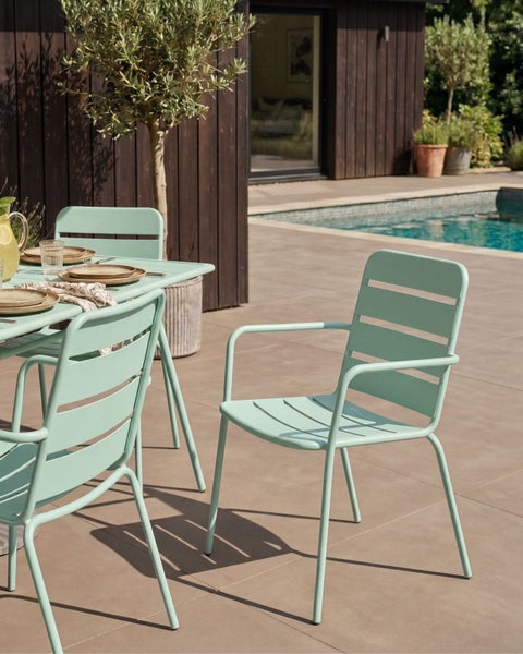Modernes, helles Gartenmöbel-Set aus Metall mit Latten-Design, bestehend aus Tisch und Stühlen auf einer gepflasterten Terrasse am Pool.
