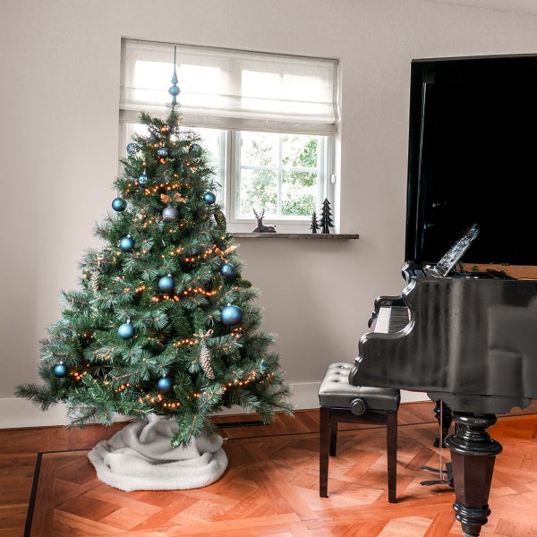 Weihnachtsbaum geschmückt mit Kugeln, Lichtern und einer Baumspitze neben einem Klavier im Raum.
