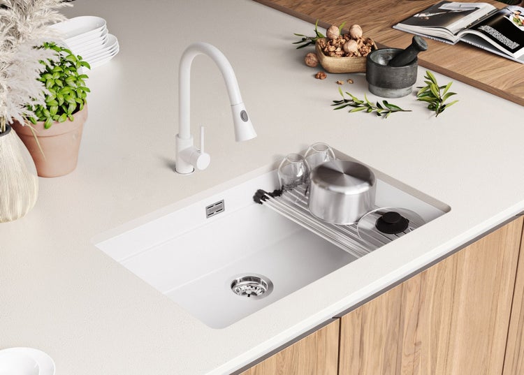 Küchenspüle mit Abtropfgestell, Wasserhahn und Geschirr auf einer Arbeitsplatte.