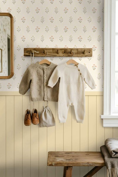 Ein Kinderzimmer mit gestreifter Blumentapete und Wandpaneelen aus Holz sowie einer rustikalen Garderobe mit hängender Kinderkleidung.
